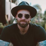 Stylish man with beard and tattoos wearing sunglasses and a hat, enjoying outdoors.